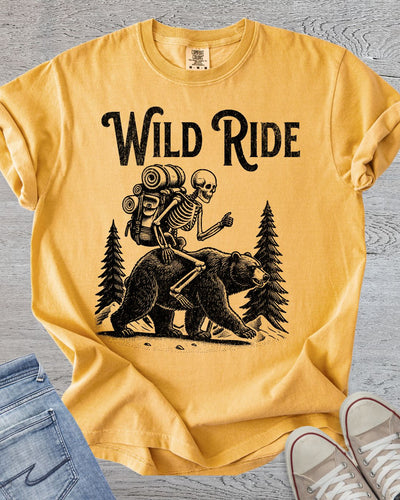 Humorous hiking tee graphic featuring skeleton riding a bear in Comfort Colors Mustard.